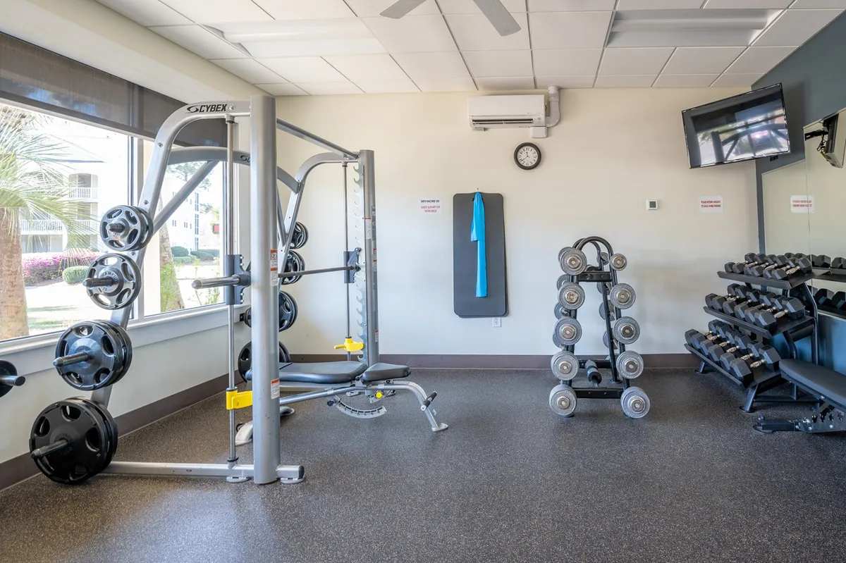A well-equipped fitness center with weightlifting stations, a dumbbell rack, and an exercise mat, all in a motivational, brightly lit setting.