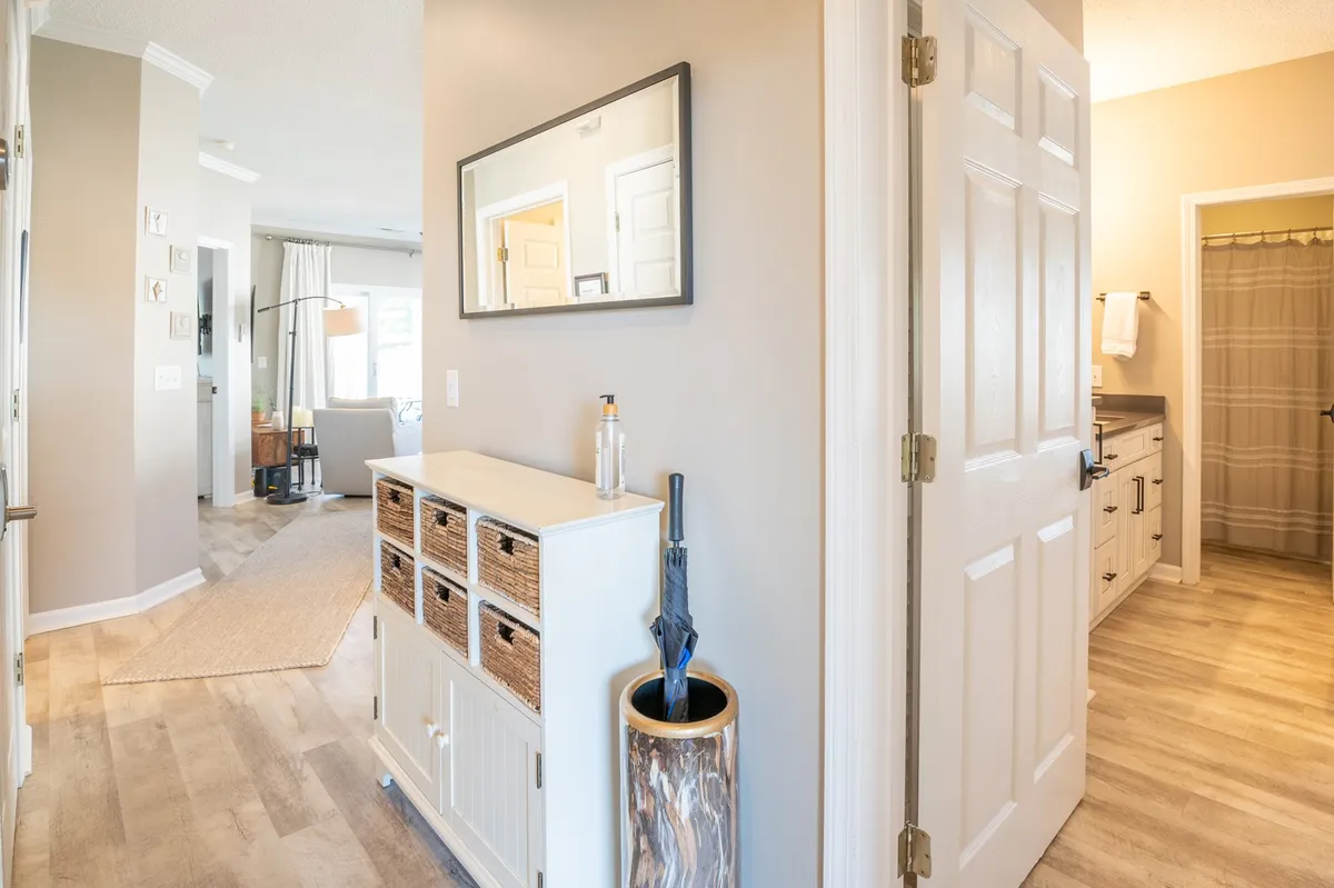 An inviting entryway featuring a console table with woven baskets, a large mirror, and decorative elements like an umbrella stand. Doorways lead to other parts of the home, hinting at a welcoming and organized environment.