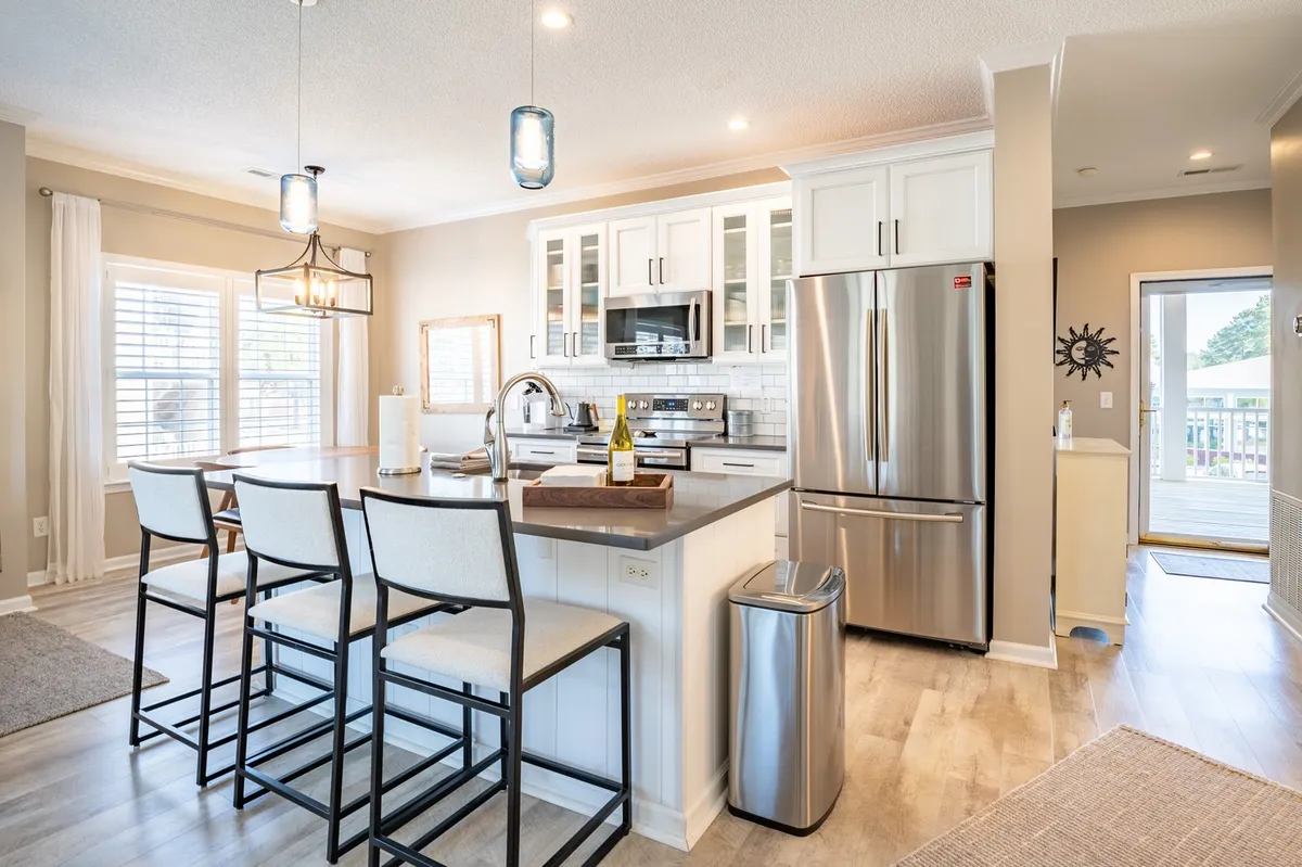 The hero image showcases a beautifully lit, open-concept kitchen and dining area with a spacious kitchen island, gleaming stainless steel appliances, and expansive windows that let in natural light. The inviting setting is ideal for cooking, entertaining, and relaxing with family or friends.