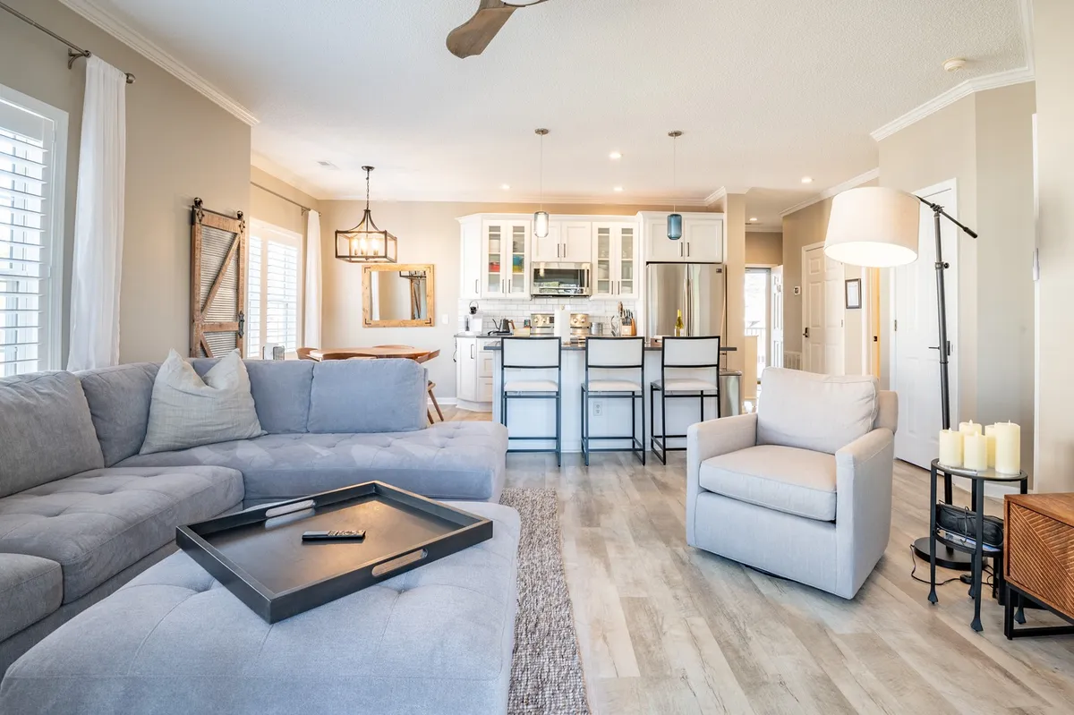 A spacious, cozy living area with a large sofa, kitchen island, and dining area, all unified in an open layout. Soft lighting, decorative candles, and a comfortable setting create a welcoming space for family relaxation or entertaining guests across all seasons.