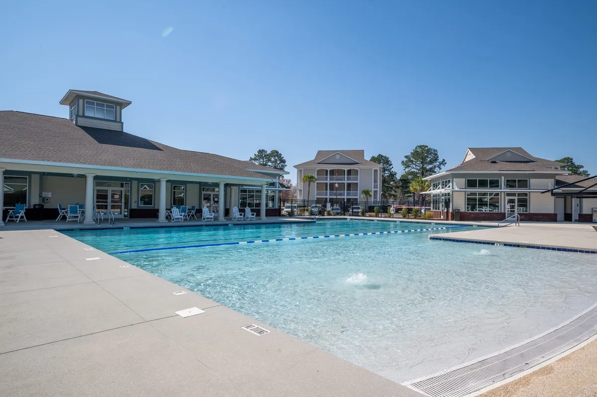 A sparkling outdoor swimming pool surrounded by lounge chairs and framed by the community’s buildings. The image conveys a relaxed, resort-like atmosphere perfect for unwinding after a day on the course or socializing with fellow guests.
