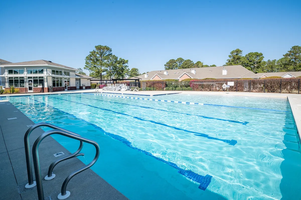 This exterior image features a sparkling swimming pool surrounded by lush greenery, with a well-appointed clubhouse and ample lounge chairs set out for relaxation. The scene conveys an active, cheerful atmosphere ideal for swimming, sunbathing, and community events.