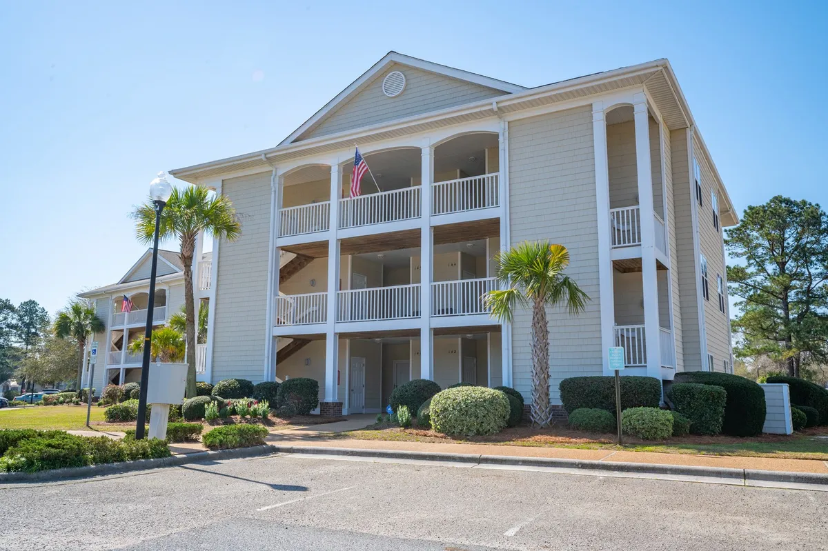 This exterior image showcases the building's facade framed by lush palm trees, with an American flag waving gently and balconies that promise elevated views. The scene is warmly lit, evoking the feeling of returning from a day at the beach or preparing to watch the sunset from your own private space.